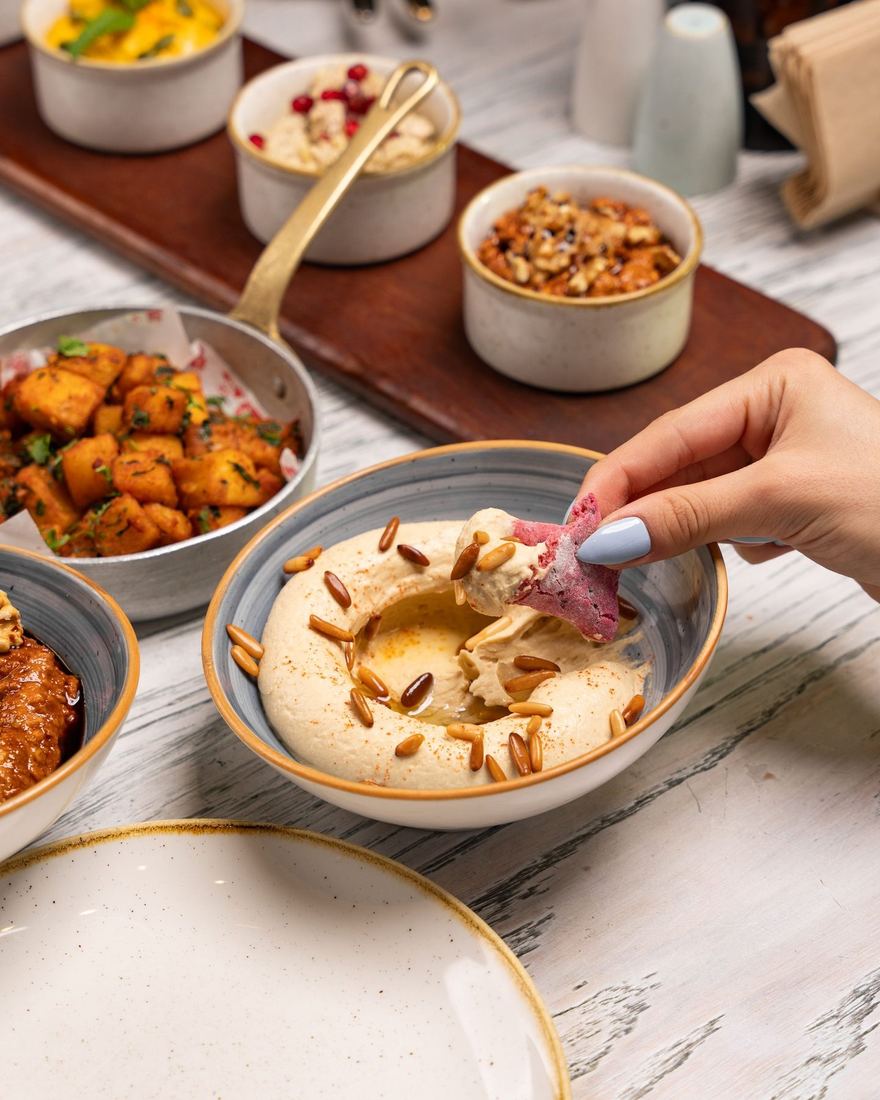 Hands dipping flatbread into a bowl of mezze